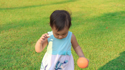 High angle view of cute girl holding ball while standing on grassy land