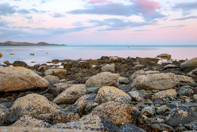 Rocks on beach against sky during sunset