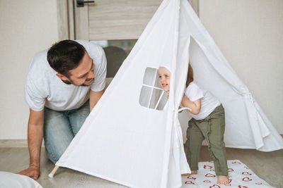 Happy father and baby girl little daughter having fun playing in wigwam in children room at home