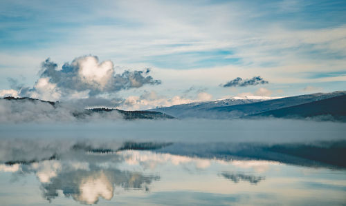 Scenic view of lake and mountains against cloudy sky during sunset