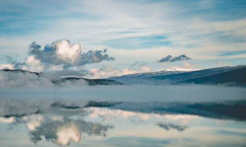 Scenic view of lake and mountains against cloudy sky during sunset