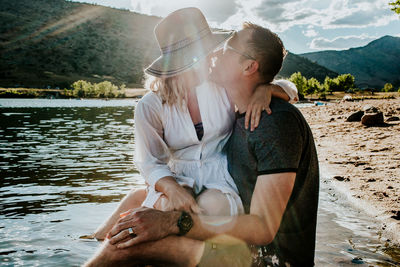 Husband and wife sitting together and kissing on lakeshore