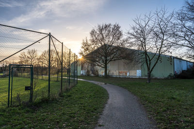 Road amidst plants and houses on field against sky