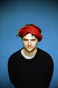 Portrait of young man wearing red turban standing against blue background