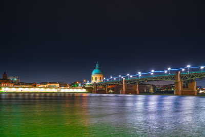 Illuminated buildings by river against sky at night