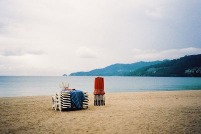 Chairs on beach chair by sea against sky