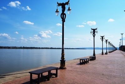 Empty street lights on pier by sea against sky