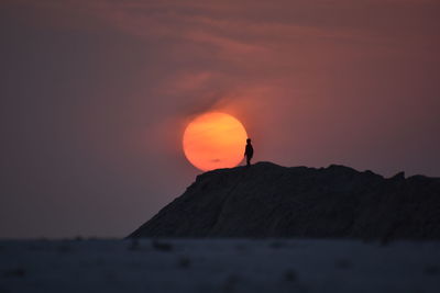 Silhouette rock in sea against sky during sunset