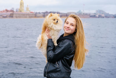 Young woman hugs spitz dog outdoors on embankment of city river in black