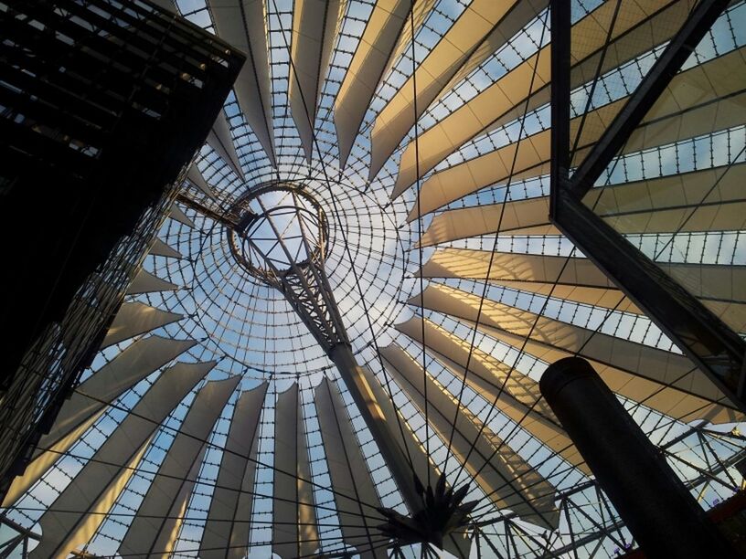 low angle view, architecture, built structure, ferris wheel, pattern, directly below, ceiling, modern, building exterior, indoors, tall - high, architectural feature, amusement park, glass - material, design, tower, skylight, amusement park ride, sky, geometric shape