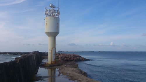 Lighthouse by sea against blue sky