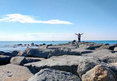 Man standing on rocks by sea against sky