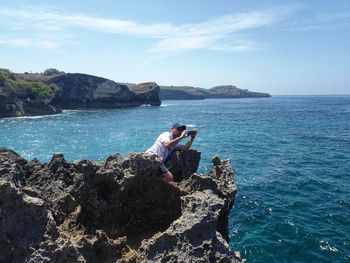 Woman on rock by sea against sky