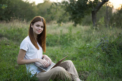 Young woman using mobile phone while sitting on field