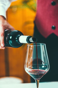 Midsection of man pouring wine in wineglass on table