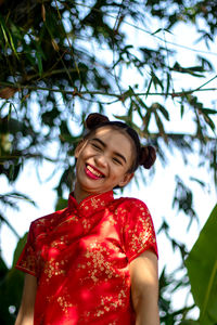 Low angle view of smiling woman against trees