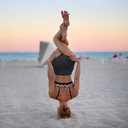 Rear view of flexible woman doing headstand on beach