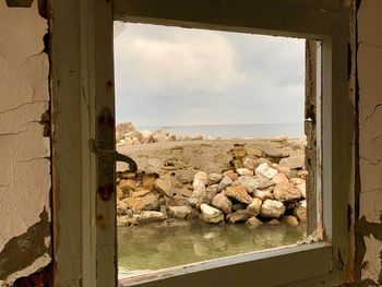 Rocks by sea against sky seen through window