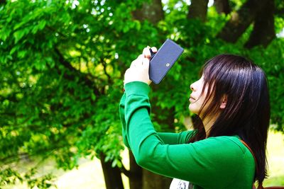 Side view of woman photographing trees in park