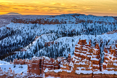 Snow covered landscape against sky during sunset