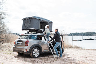 Father helping his daughter climb a ladder to a roof top tent camping