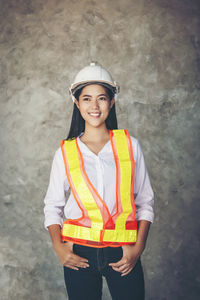 Portrait of a smiling young woman standing against wall