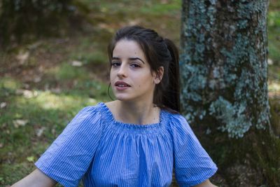 Portrait of young woman sitting by tree