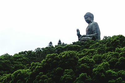 Low angle view of statue against trees against clear sky