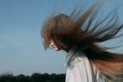 Woman with tousled hair against sky