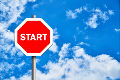 Low angle view of start text on road sign against blue sky