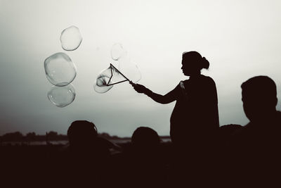 Silhouette people with bubbles against clear sky during sunset