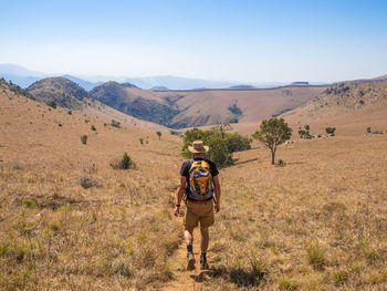 Full length rear view of man walking on field against mountains