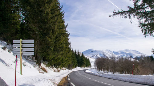 Road amidst trees and snowcapped mountains against sky