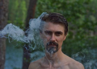 Portrait of shirtless young man standing against trees