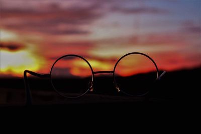 Close-up of sunglasses against sky during sunset