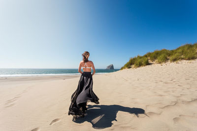 Rear view of woman standing on beach against clear sky