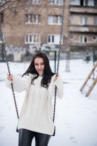 Portrait of young woman swinging in snow covered playground