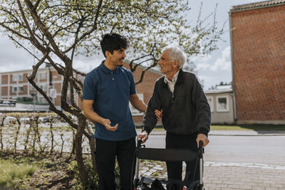 Smiling male caregiver assisting senior man with walker on footpath