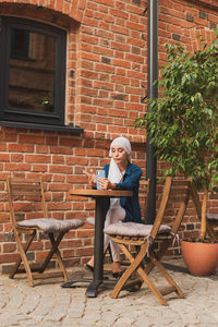 Woman sitting on chair against brick wall