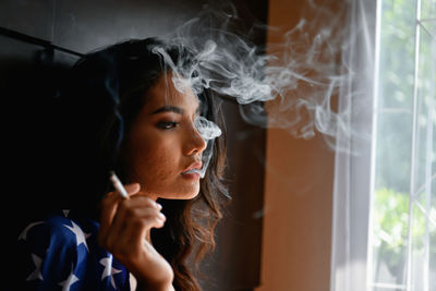 Side view of young woman smoking cigarette at home