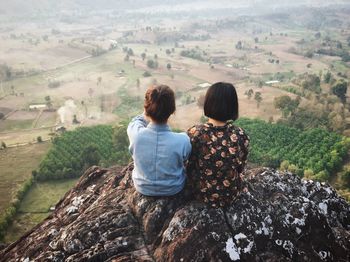 Rear view of friends looking at landscape while sitting on mountain