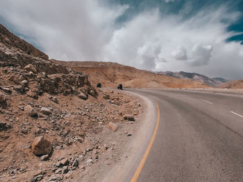 Road passing through desert against cloudy sky
