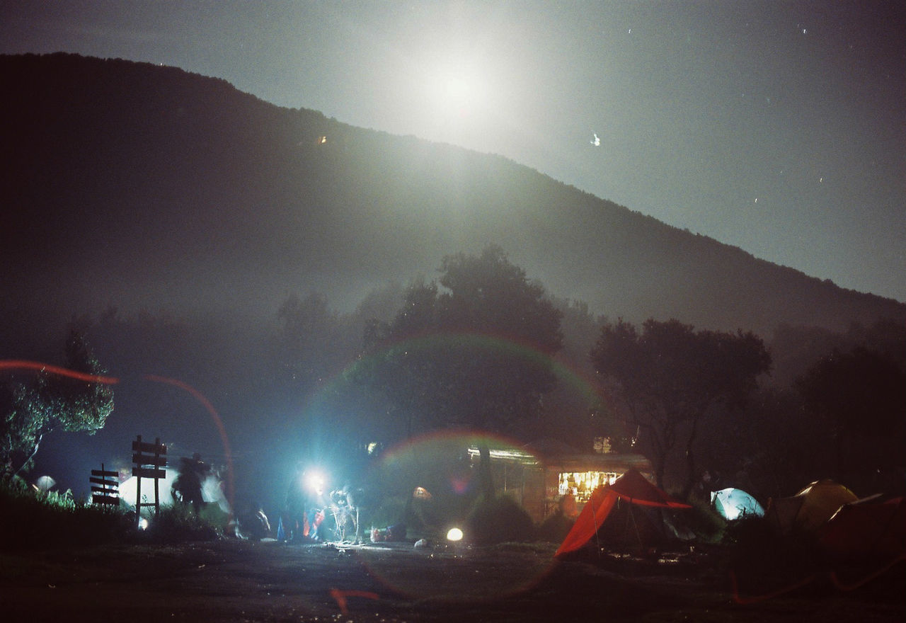 illuminated, night, sky, tree, lens flare, nature, architecture, group of people, mountain, lighting equipment, plant, city, outdoors, glowing, built structure, building exterior, crowd, real people, festival