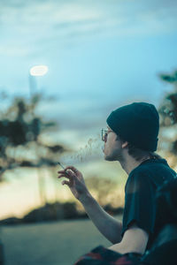 Side view of man smoking looking at sunset