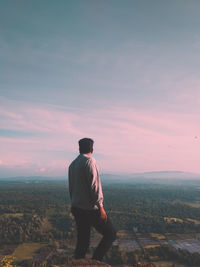 Rear view of man standing on landscape against sunset sky