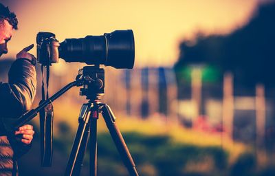 Side view of male photographer photographing with camera during sunset