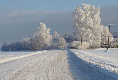 Snow covered road by trees against sky