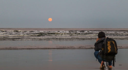 Rear view of woman standing on beach against clear sky