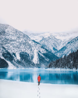 Rear view of man walking by lake against sky