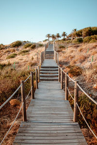 Boardwalk leading towards footbridge against clear sky